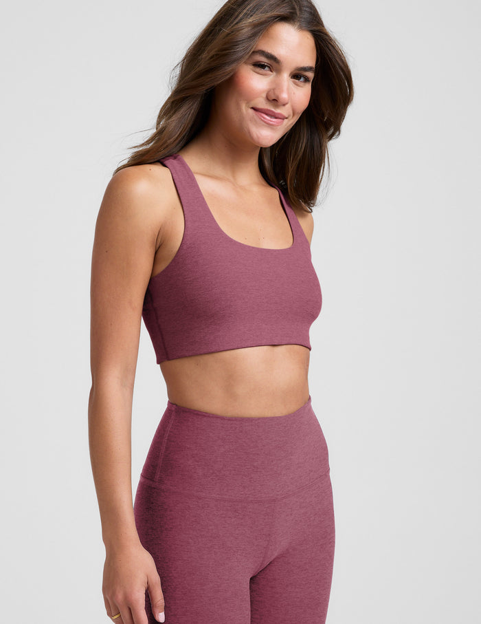 Woman wearing a purple sports bra and leggings on a light gray background.