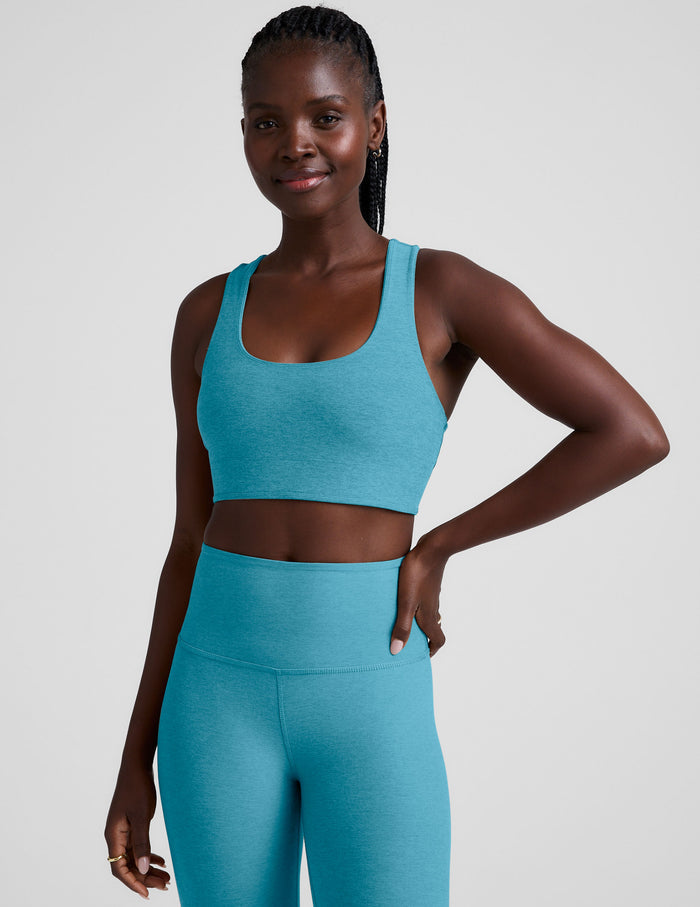 Woman wearing a blue long line racerback sports bra and leggings on a plain background.