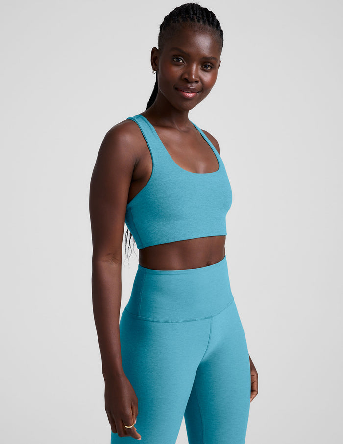 Woman wearing a blue long line racerback sports bra and leggings on a plain background.