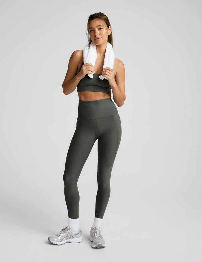 Woman wearing a green bra and leggings on a light gray background.