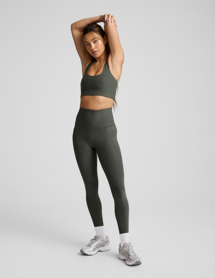 Woman wearing a green bra and leggings on a light gray background.
