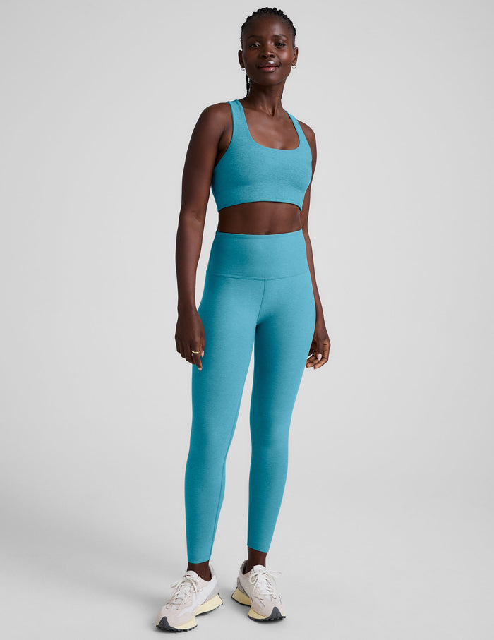 Woman wearing a blue long line racerback sports bra and leggings on a plain background.