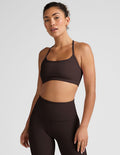 Woman wearing a brown racerback sports bra and leggings on a light gray background.