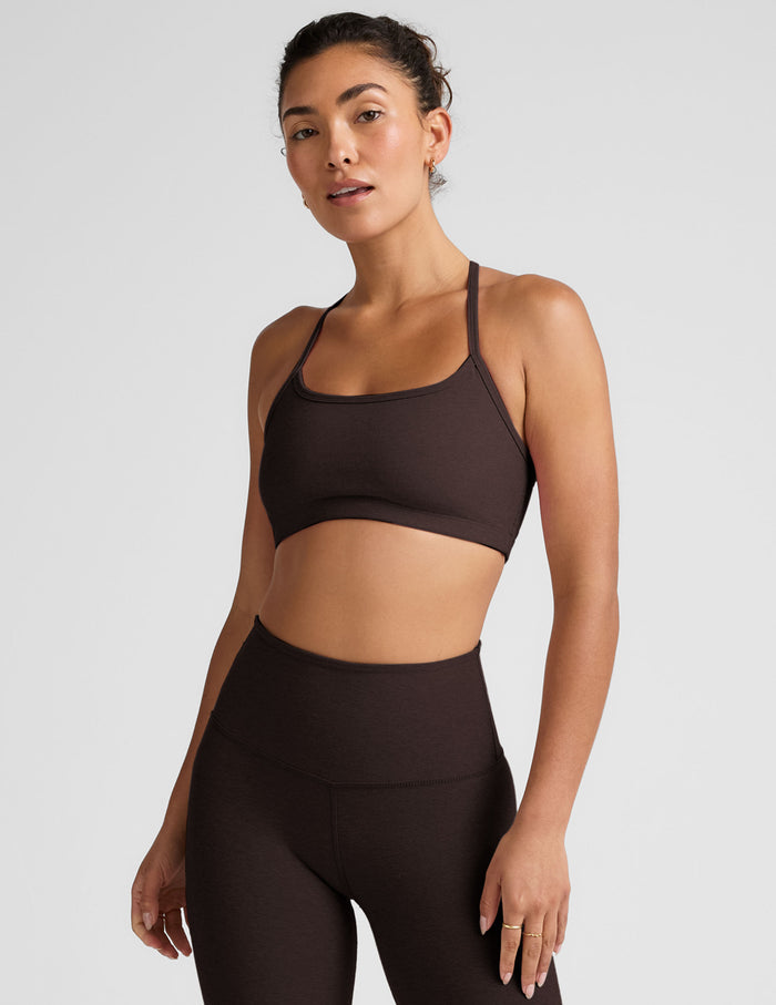 Woman wearing a brown racerback sports bra and leggings on a light gray background.
