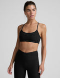 Woman wearing a black sports bra and leggings on a light gray background.