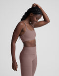 Woman wearing a brown sports bra and leggings on a light gray background.