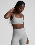 Woman wearing a gray sports bra and leggings on a light gray background.