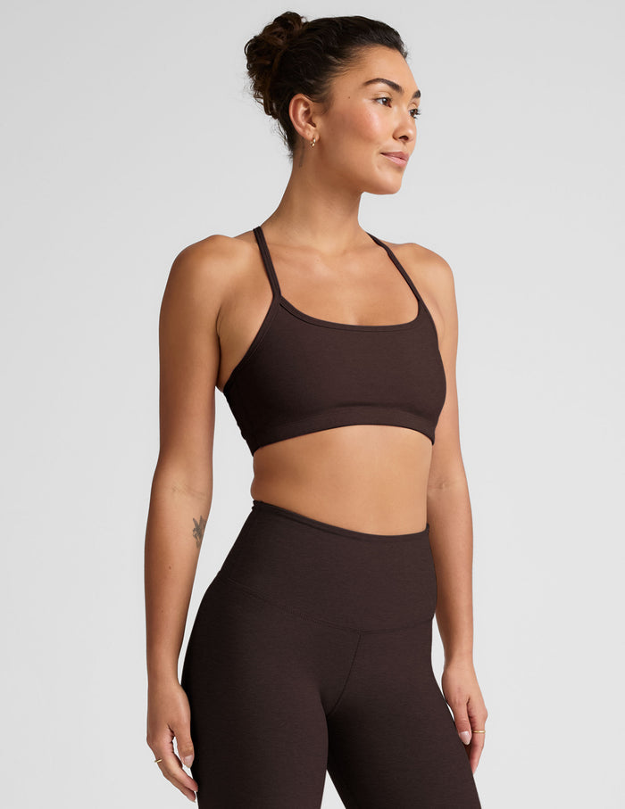 Woman wearing a brown racerback sports bra and leggings on a light gray background.