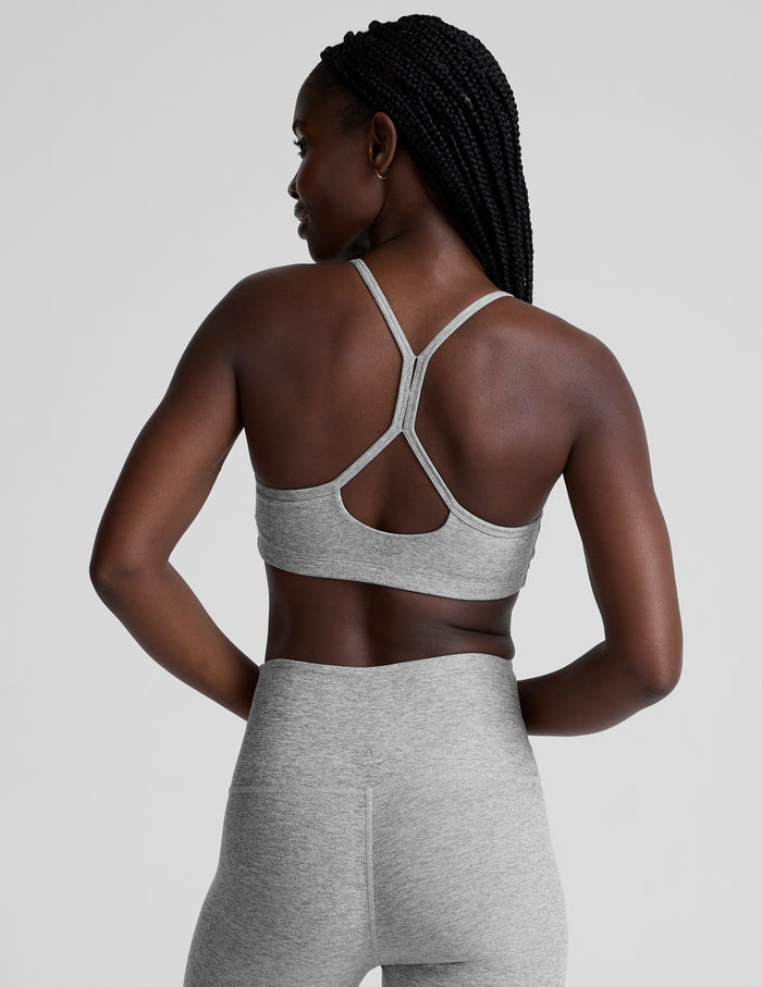 Woman wearing a gray sports bra and leggings on a light gray background.