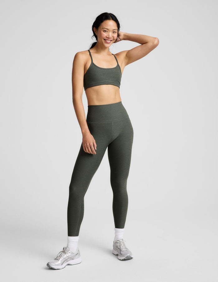 Woman wearing a green sports bra and leggings on a light gray background.
