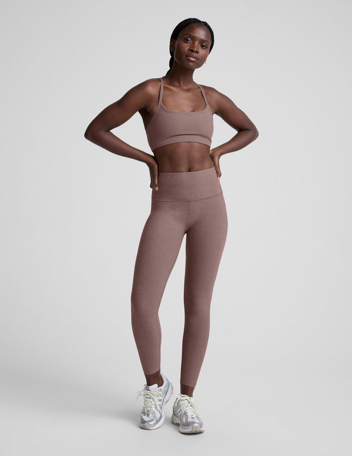 Woman wearing a brown sports bra and leggings on a light gray background.