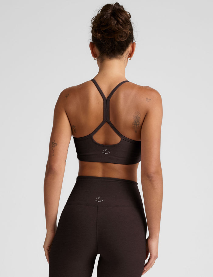 Woman wearing a brown racerback sports bra and leggings on a light gray background.