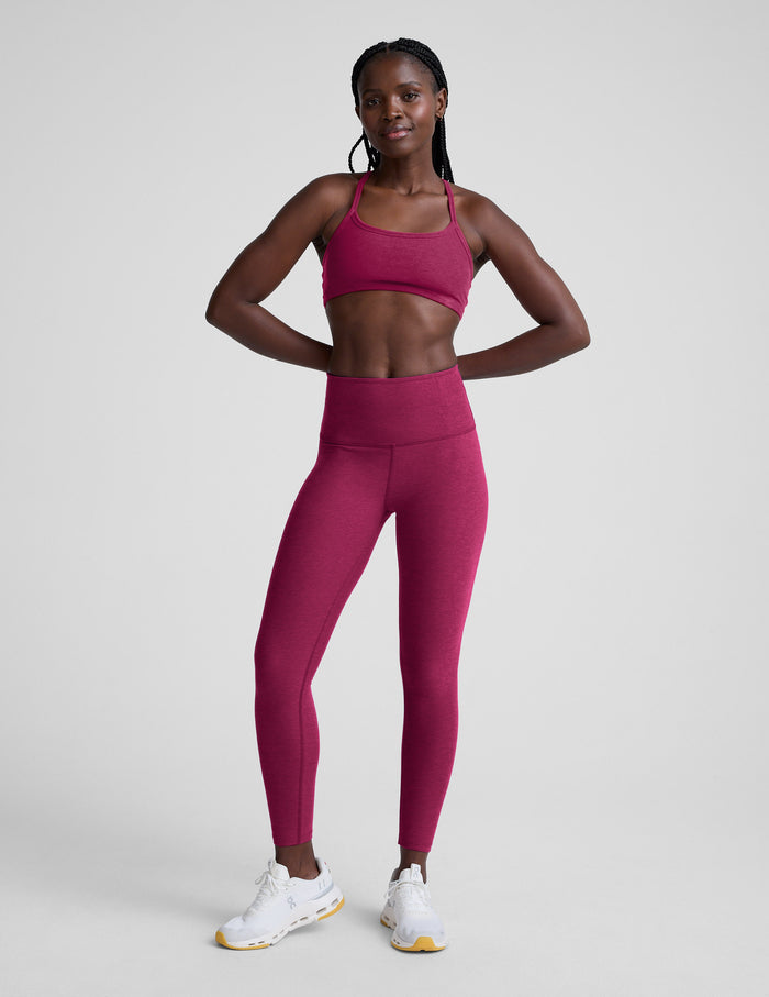 Woman wearing a red sports bra and leggings on a light gray background.