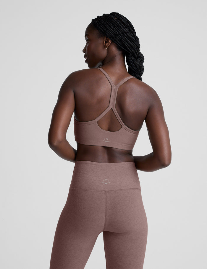 Woman wearing a brown sports bra and leggings on a light gray background.