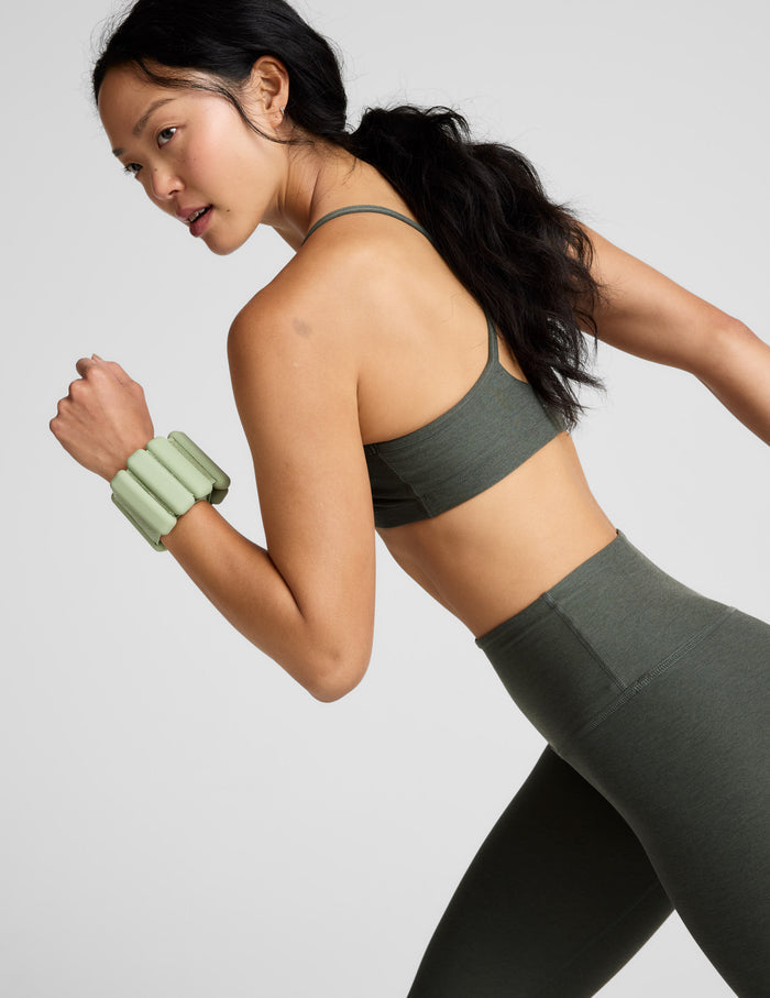 Woman wearing a green sports bra and leggings on a light gray background.