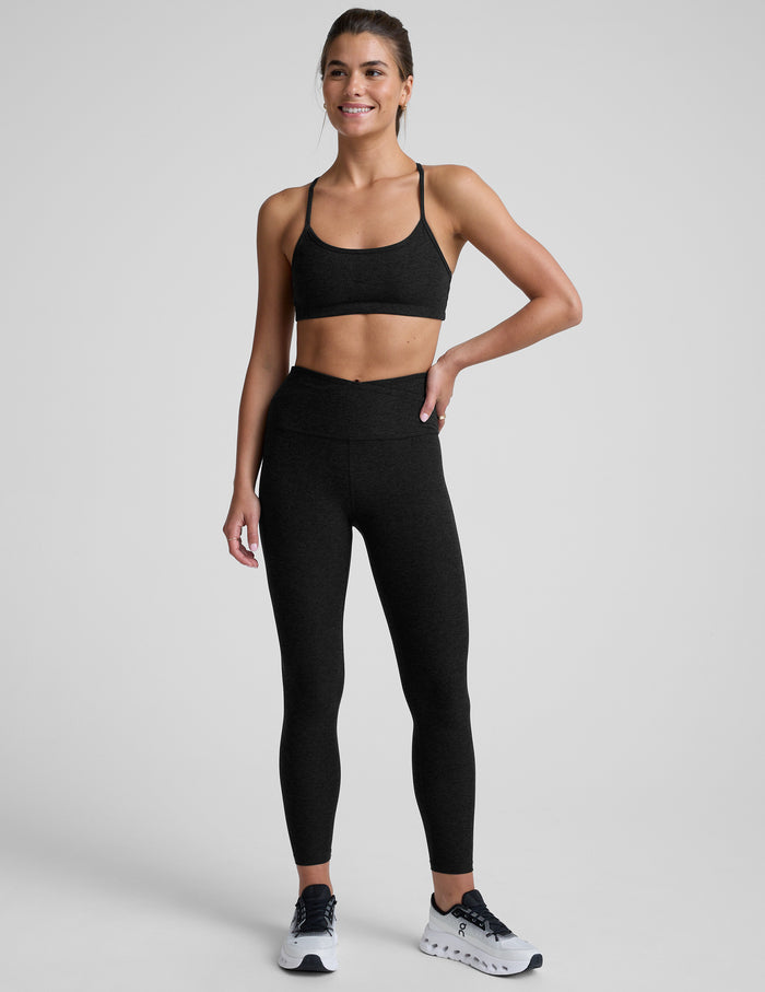 Woman wearing a black sports bra and leggings on a light gray background.