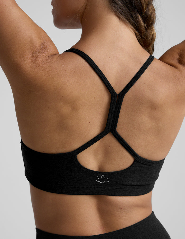 Woman wearing a black sports bra and leggings on a light gray background.