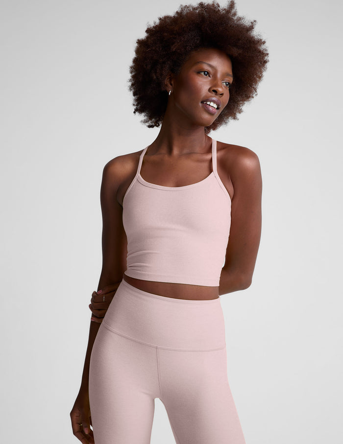Woman wearing a pink racerback cropped tank and leggings on a light gray background.