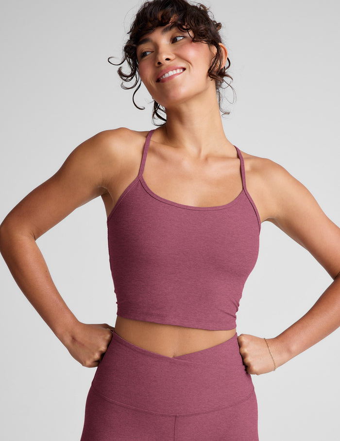 Woman wearing a purple racerback cropped tank and leggings against a plain background.