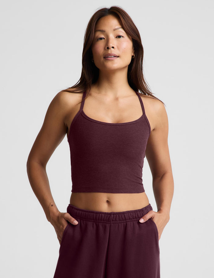 A woman modeling a matching athletic set consisting of a dark burgundy cropped tank top and matching sweatpants against a light gray studio background.