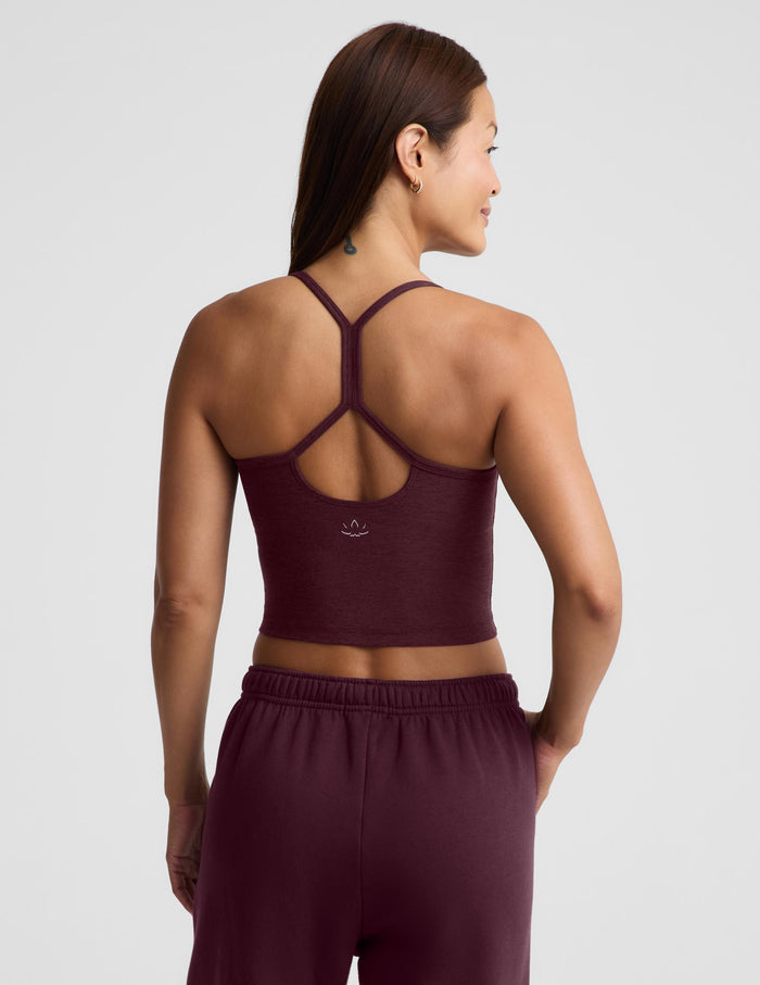 A woman modeling a matching athletic set consisting of a dark burgundy cropped tank top and matching sweatpants against a light gray studio background.