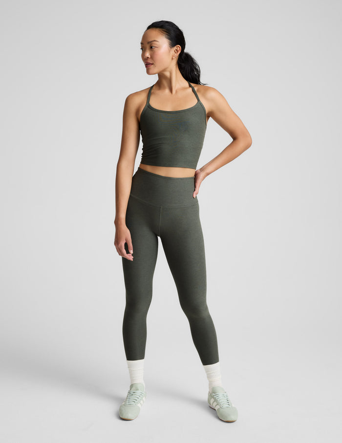 Woman wearing a green racerback cropped tank and leggings against a plain background.