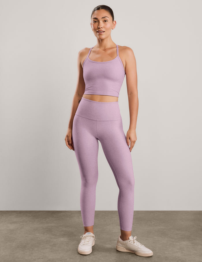A woman modeling a matching light purple athletic set consisting of a scoop-neck cropped tank and high-waisted leggings, posed against a solid light gray background.