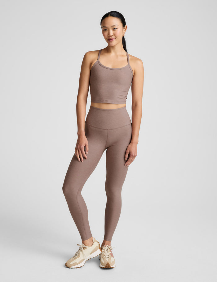 Woman in a brown tank top and leggings  against a plain background.