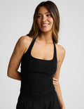 Woman wearing a black halter tank and black pants against a plain background.