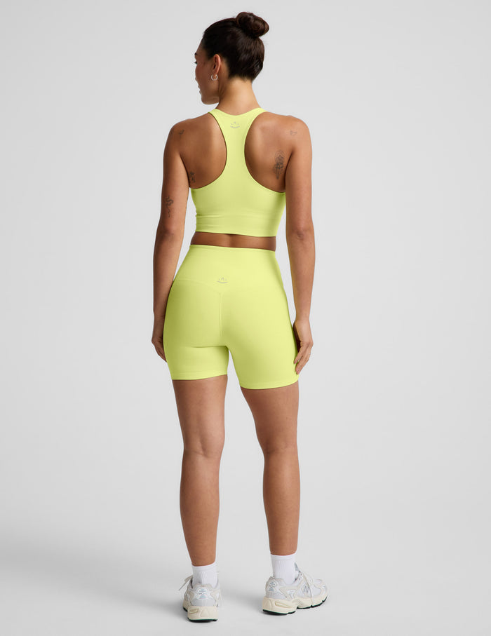 Woman wearing Yellow Spacedye™ Streamline 5" Short, paired with a matching tank and sneakers. Rear view.