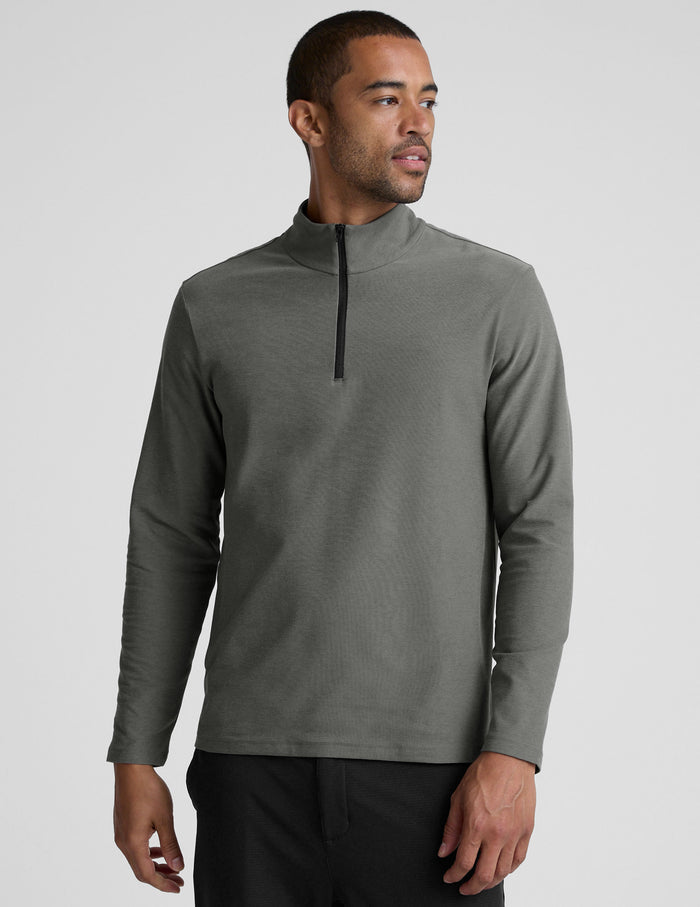 man wearing a gray quarter zip pullover with black pants and a plain background.
