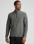 man wearing a gray quarter zip pullover with black pants and a plain background.