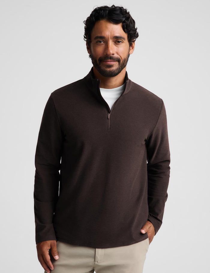 A man wearing a dark brown quarter-zip long-sleeve knit pullover over a white t-shirt and khaki pants, standing against a light gray studio background.