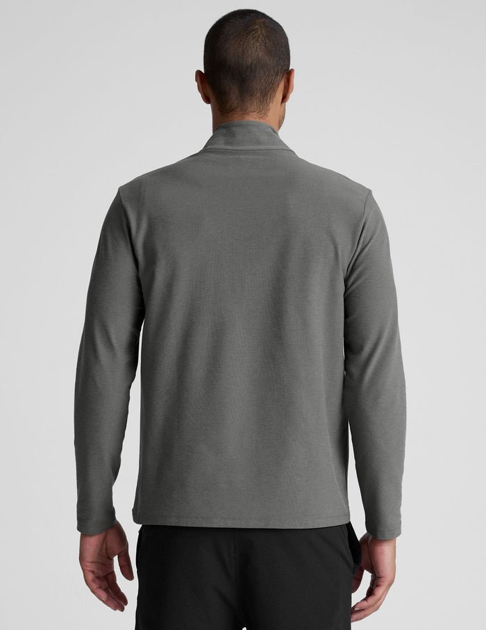 man wearing a gray quarter zip pullover with black pants and a plain background.