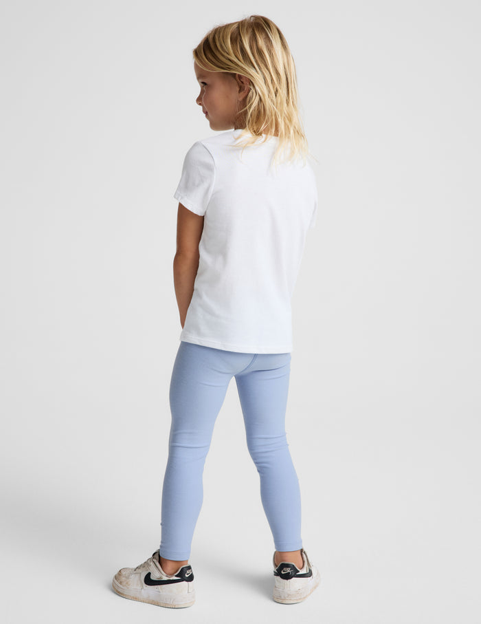 Girl wearing Blue Spacedye™ Toddler Legging paired with a white t-shirt and white sneakers, rear view.
