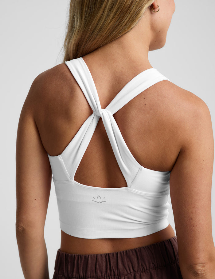 A woman shown from the back wearing a white athletic crop top with a crossover crisscross strap design at the neckline.