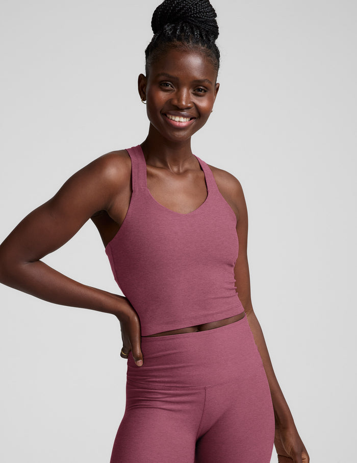 Woman wearing a purple cropped tank with twist back strap details and leggings against a plain background.