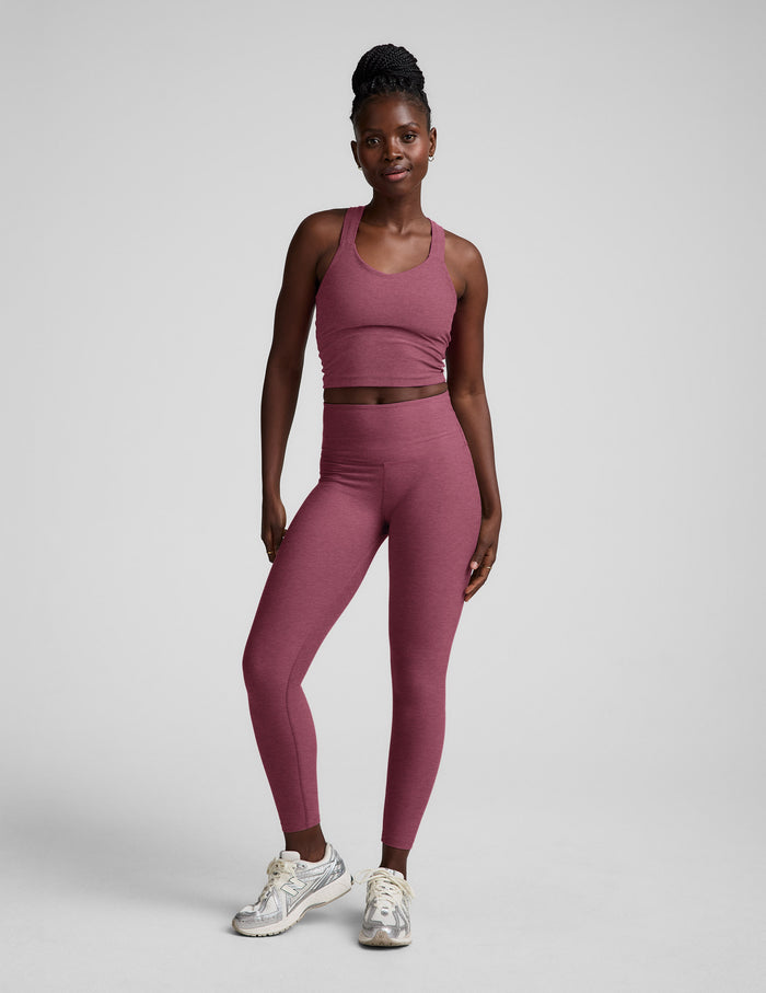 Woman wearing a purple cropped tank with twist back strap details and leggings against a plain background.