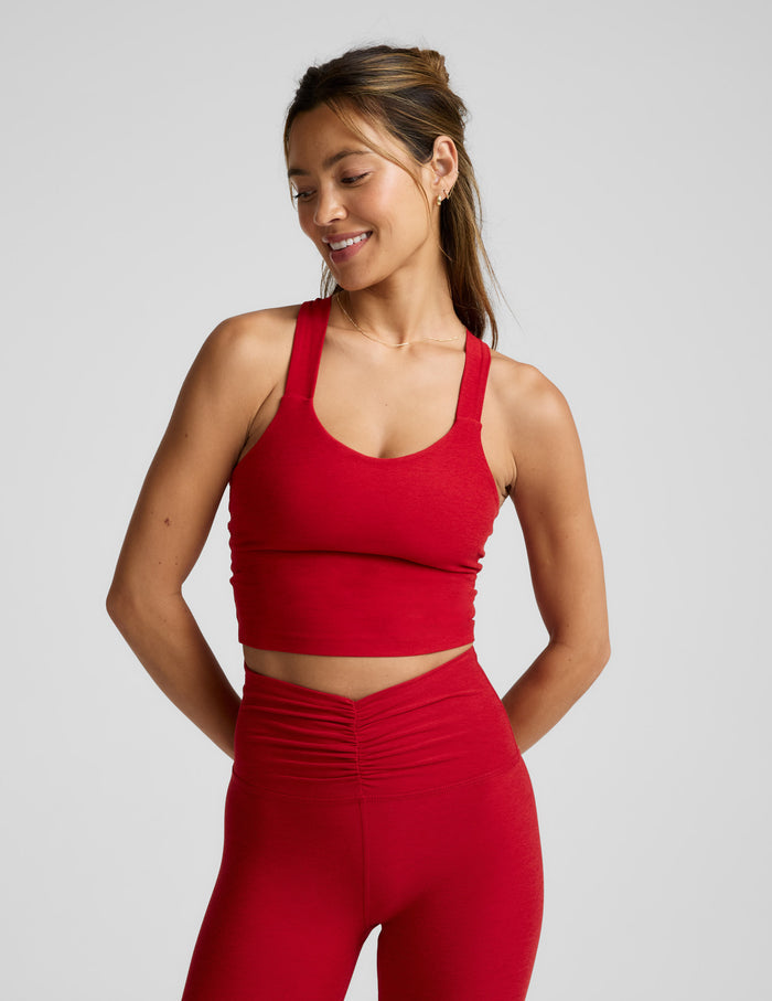 Woman wearing a red cropped tank with twist back strap details and leggings against a plain background.
