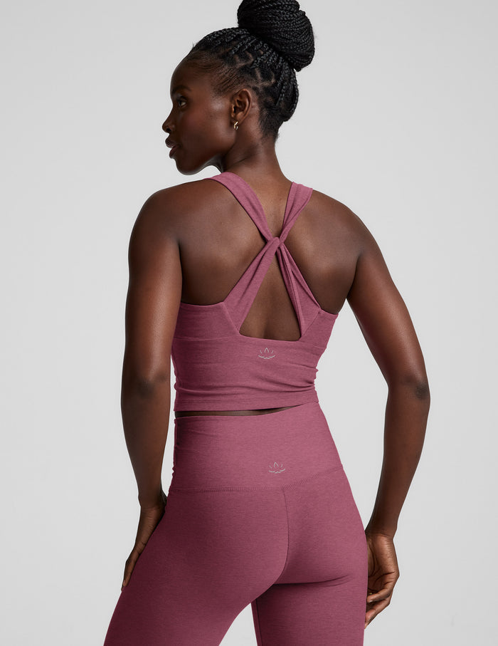 Woman wearing a purple cropped tank with twist back strap details and leggings against a plain background.