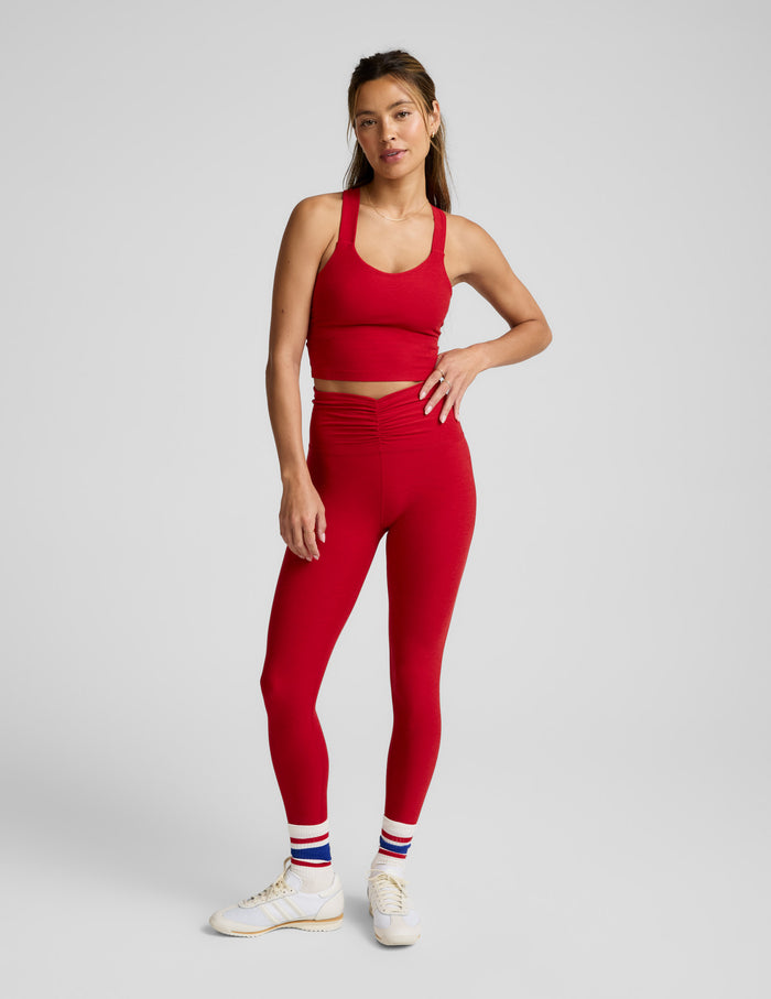 Woman wearing a red cropped tank with twist back strap details and leggings against a plain background.