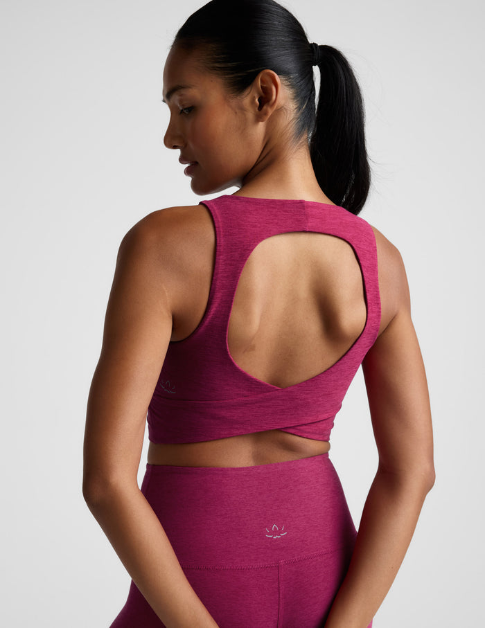 Woman wearing a red cropped tank top with a crossover back detail and matching leggings against a light gray background.