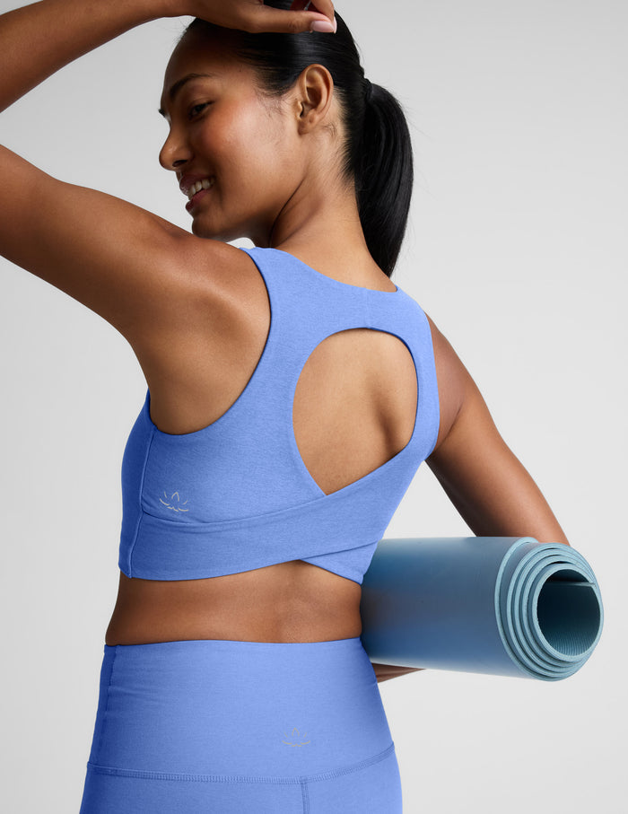Woman wearing a blue cropped tank with a crossover back detail and blue leggings against a plain background.