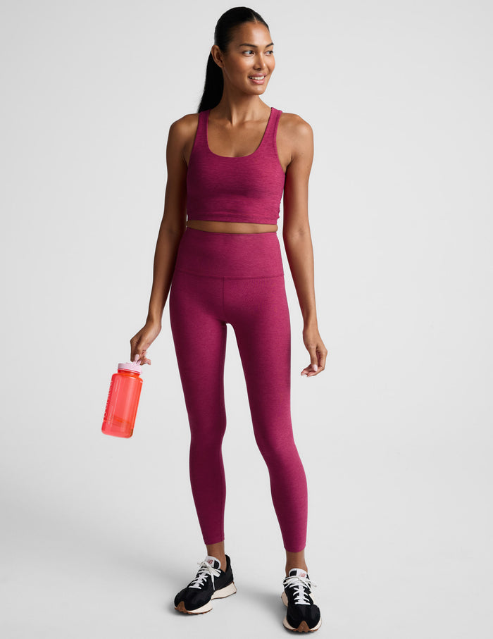 Woman wearing a red cropped tank top with a crossover back detail and matching leggings against a light gray background.