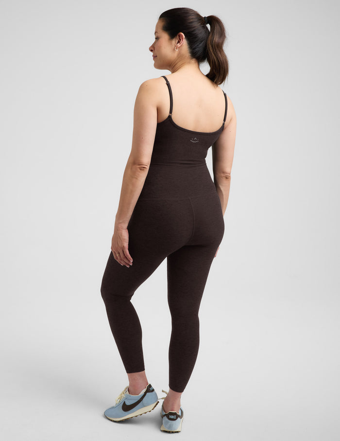 Pregnant woman wearing a brown midi length jumpsuit against a plain background.