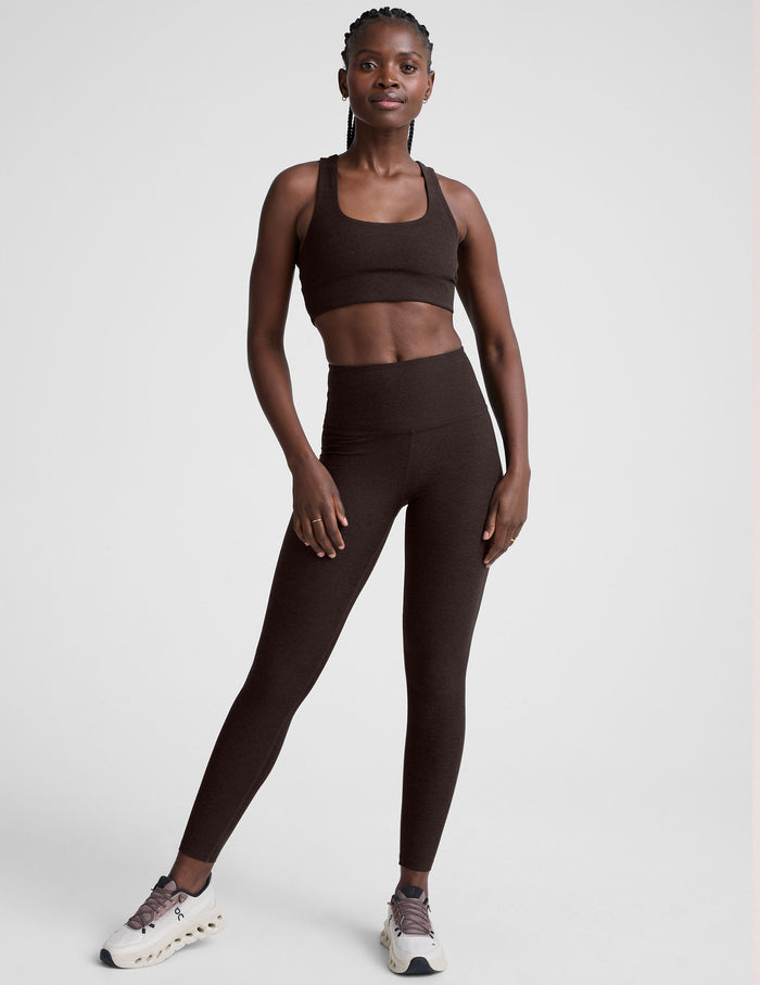 woman wearing a brown sports bra and long leggings set on a white background.