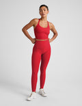 Woman wearing a red cropped tank and high-waisted full length leggings on a plain background.