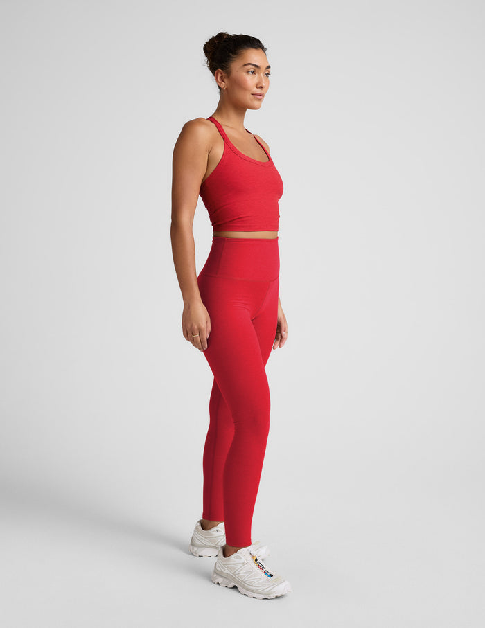 Woman wearing a red cropped tank and high-waisted full length leggings on a plain background.