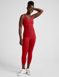 Smiling woman wears red Spacedye Walk And Talk High Waisted Capri Legging with matching tank top and white sneakers.