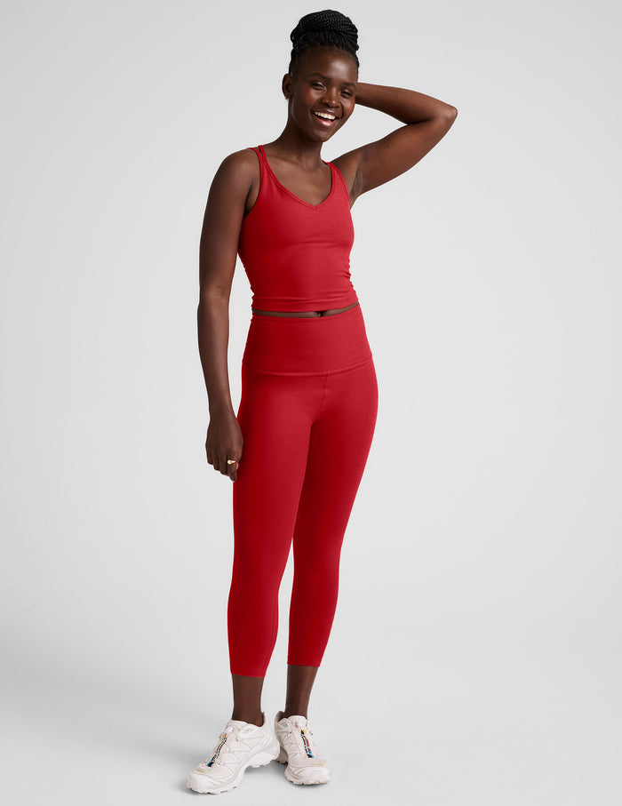 Smiling woman wears red Spacedye Walk And Talk High Waisted Capri Legging with matching tank top and white sneakers.
